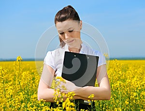 Sad business woman in flower field outdoor with clipboard. Young girl in yellow rapeseed field. Beautiful spring landscape, bright