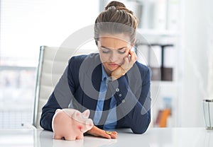 Sad business woman with piggy bank looking on coin