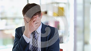 Sad businessman in suit covering face with his hand in office