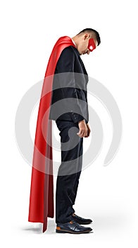 A sad businessman in a superhero red cape standing with his shoulders slumped and looking down.
