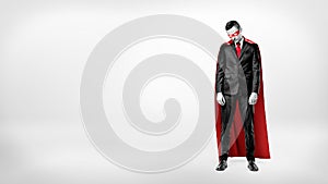 A sad businessman in a superhero red cape standing on white background with his shoulders slumped.