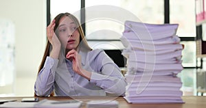 Sad businesswoman or intern looking at large stack of document folders at workplace