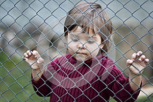 Sad child behind fence