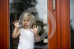 Sad child behind the window on rainy day