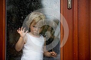 Sad child behind the window on rainy day