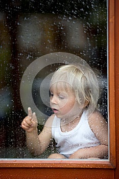Sad child behind the window on rainy day