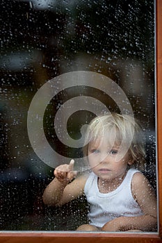 Sad child behind the window on rainy day
