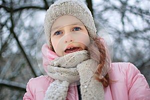 Sad child girl in warm knitted winter clothes spent time outdoors and got frozen.