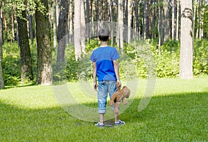 Sad child is holding a brown teddy bear and standing on the meadow. Back view. Copy space. Sadness, fear, frustration