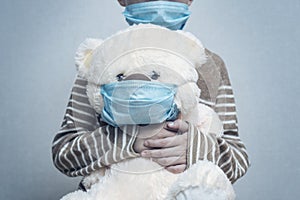 A sad child holds his teddy bear, both wearing protective medical masks. Coronavirus quarantine. Prevention epidemic