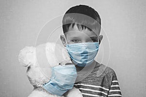 A sad child holds his teddy bear, both wearing protective medical masks. Coronavirus quarantine. Prevention epidemic