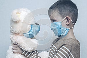 A sad child holds his teddy bear, both wearing protective medical masks. Coronavirus quarantine. Prevention epidemic