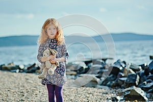 Sad child hugs toy on the shore of the pond
