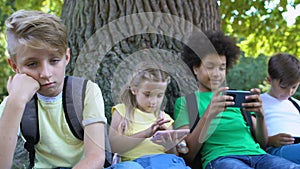 Sad child looking at friends scrolling smartphones feeling bored, communication