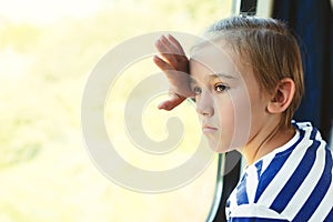 Sad child looking out the train window. Kid travels on a train. Little boy is traveling on the train
