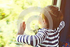 Sad child looking out the train window. Kid travels on a train. Little boy is traveling on the train