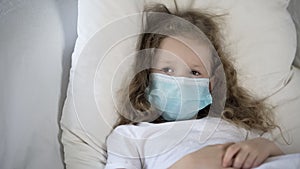 Sad child in medical face mask lying in bed, suffering rare disease, epidemic