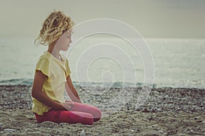 Sad child sitting alone in sandy beach near the sea