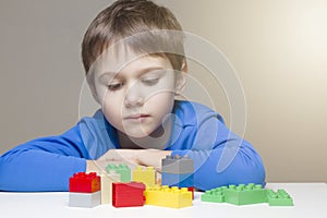 Sad child sitting and looking to colourful plastic construction toy blocks at the table