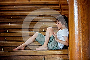 Sad child, sitting on a staircase in a big house, concept for bu