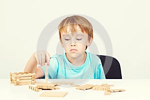 Sad child sitting at table. Child plays with construction toy blocks at the table. Sad bored boy build wooden house. Kid plays wit