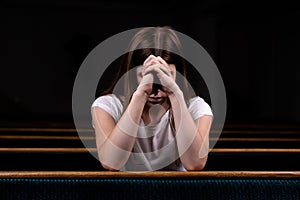 A Sad Christian girl in white shirt is sitting and praying with humble heart in the church