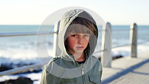 Sad, cold and face of a child at the beach, walking and angry on a holiday at the promenade in Portugal. Unhappy, lonely