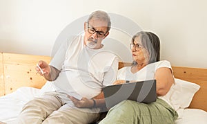 Sad confused old caucasian husband and wife lie on bed, pay for bills, taxes