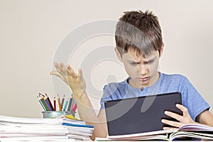 Sad, confused,surprised child with tablet computer sitting at table with books notebooks