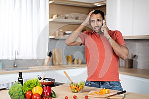 Sad confused young african american guy in red t-shirt holds his head with hand calls by phone, got bad disturbing news