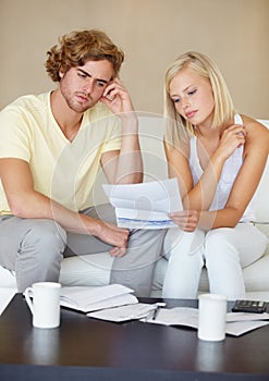 Sad couple, bills and documents stress on sofa in debt, financial planning and budget risk or worry at home. Young woman