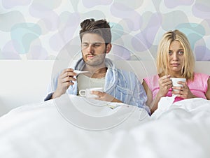 Sad couple holding coffee mugs while relaxing on bed