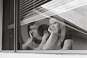 Sad couple looking out from home window