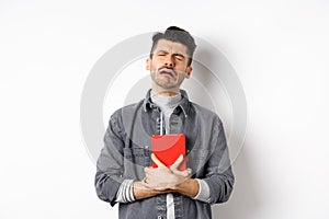 Sad cryig man holding red diary and sobbing, miserable guy carry journal with him, standing against white background