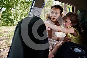 Sad baby girl on the child`s car seat pointing her finger and showing her mother to something outside the car