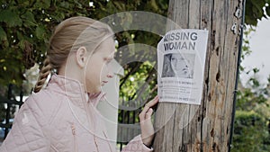 A sad, crying child stands at an ad for a missing woman.