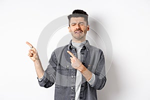 Sad crying man pointing fingers left at logo, sobbing and whining, being jealous or upset, standing on white background