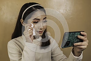 Sad crying teen girl checking her phone sitting. Asian woman staring at smartphone screen shedding tears