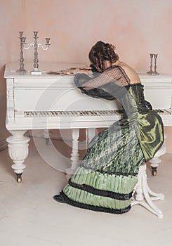 Sad crying woman wearing green medieval vintage Victorian Style dress near piano