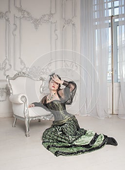 Sad crying woman wearing medieval vintage Victorian Style dress sitting on the floor near armchair