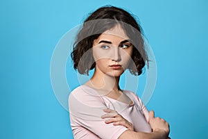 sad curly young brunette woman on blue background.