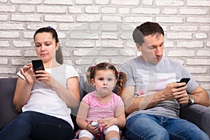 Sad Daughter Sitting Between Parents Using Mobilephone