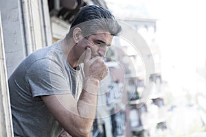 sad and depressed 40s man looking through outdoors at home balco