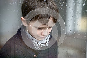 Sad depressed 7 year old boy standing by the window