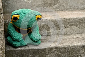 Sad depressed abandoned green frog plush toy plushie sitting on the stairs alone, feeling down, sadness, depression, alienation,