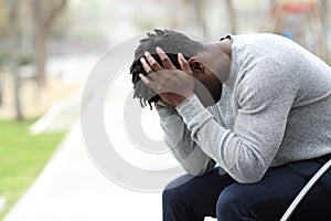 Sad depressed black man on a bench in a park