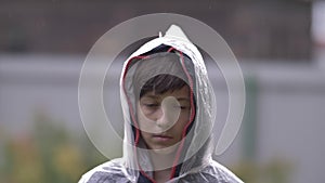 Sad depressed boy standing in a raincoat in the rain, slow motion