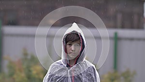 Sad depressed boy standing in a raincoat in the rain, slow motion