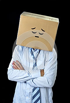 Sad and depressed businessman wearing cartoon smiley face painted on cardboard box over his head