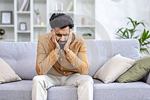 Sad depressed man sitting at home on sofa in living room, hopelessly lonely